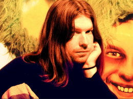 A man (Aphex Twin) with long hair in front of a painting