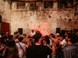 crowd of people dancing in front of a dj in a warehouse at bridge festival