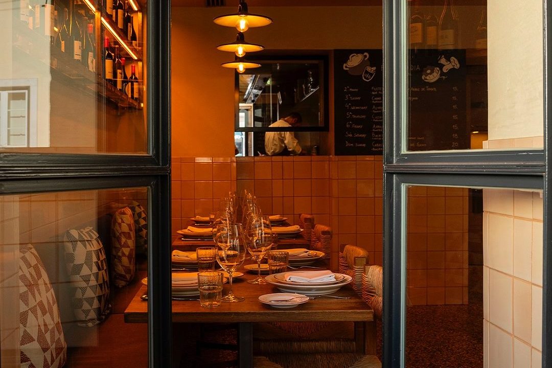 Warm, intimate dining space at Pica-Pau restaurant in Lisbon, with soft lighting, wooden tables, and neatly arranged wine glasses