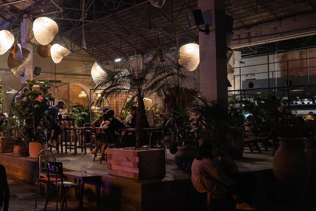 Dimly lit seating area at 8 Marvila, Lisbon, featuring hanging lamps, plants, and a relaxed nighttime atmosphere.