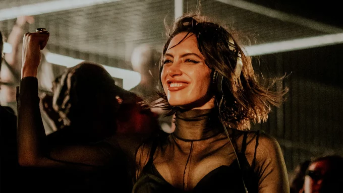 Sara Landry smiling mid-set with headphones on, wearing a sheer black outfit as the crowd dances behind her.