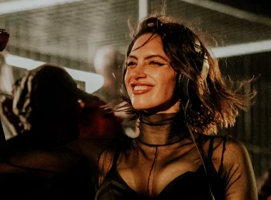 Sara Landry smiling mid-set with headphones on, wearing a sheer black outfit as the crowd dances behind her.