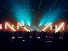 Vibrant crowd gathered at Meeraqui event in a historic venue, illuminated by colorful lights and lasers during an electronic music performance.