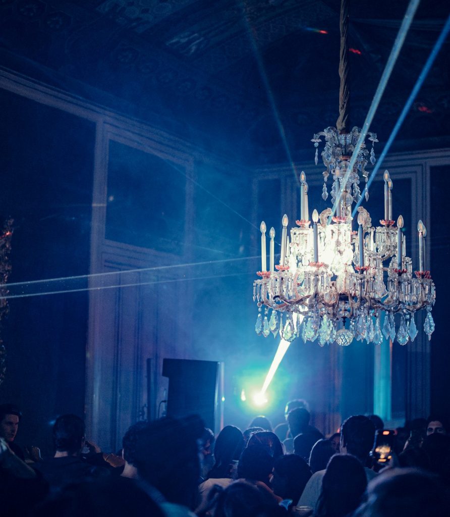 Spectacular chandelier with laser beams cutting through the room at a Meeraqui event, creating an elegant yet energetic vibe in a historic venue.