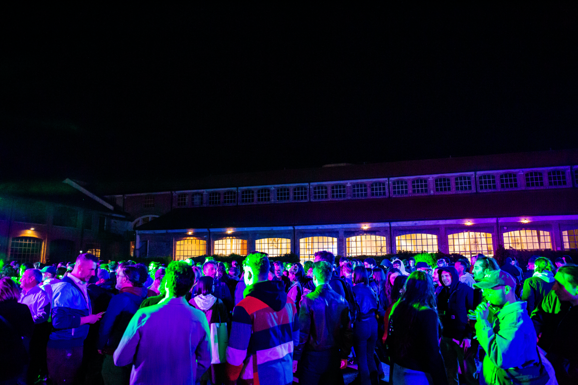 Crowd gathered at Fabbrica del Vapore during Fabbrica Design Week 2025, illuminated by vibrant stage lights against a backdrop of industrial architecture