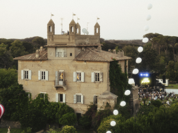 A wide view of the SUPERAURORA Festival venue set at a 17th-century castle, surrounded by lush nature. The crowd is enjoying the performance with the castle in the background, illuminated by soft lighting that creates an immersive festival atmosphere.