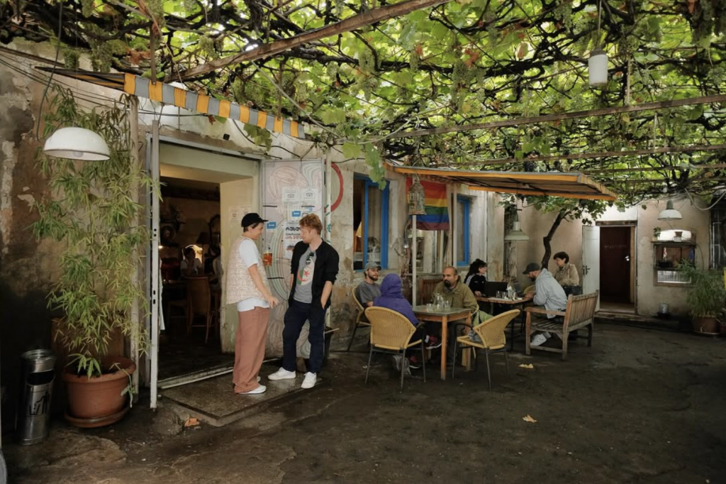 Queer-friendly café courtyard in Tbilisi with lush vines, relaxed atmosphere, and local crowd at Sophia Melnikova’s Fantastic Doukan.
