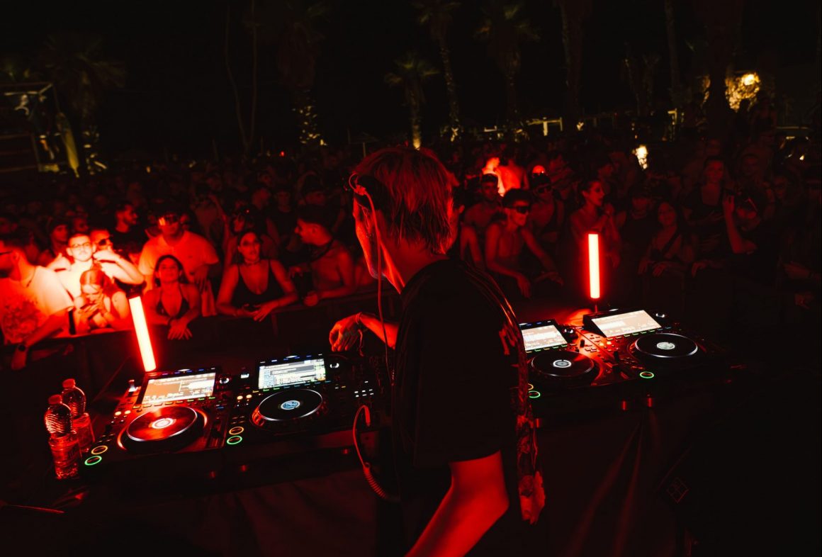 a red and black filtered photo from a club with DJ playing for the crowd at an event by XCEED