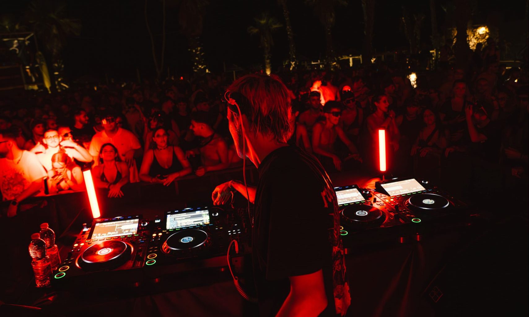 a red and black filtered photo from a club with DJ playing for the crowd at an event by XCEED