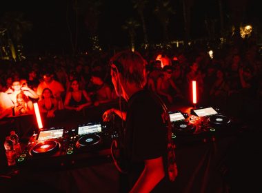 a red and black filtered photo from a club with DJ playing for the crowd at an event by XCEED