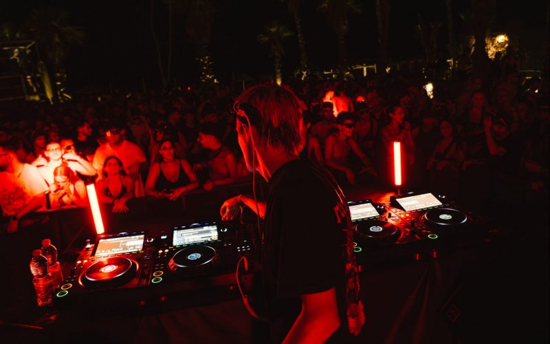 a red and black filtered photo from a club with DJ playing for the crowd at an event by XCEED