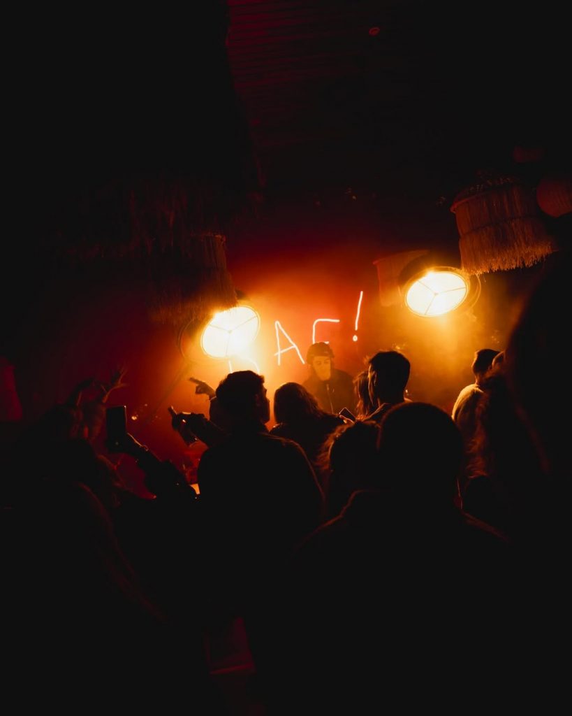 Crowd dancing at a BAF! Barcelona with red lighting and a glowing BAF! sign behind the DJ booth, creating a warm and intimate atmosphere