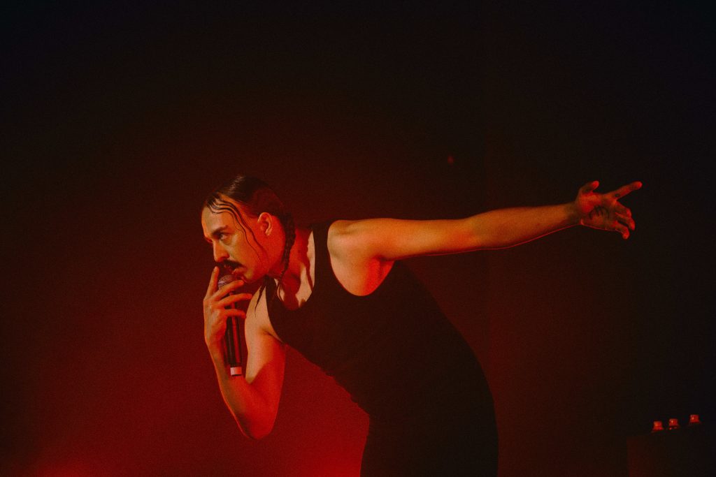 Performer Tommy Cash on stage at VIDEOCITTÀ in dramatic red lighting during live set.