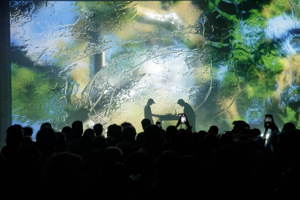 Silhouetted live A/V performance against a vibrant projection-mapped backdrop at VIDEOCITTÀ.