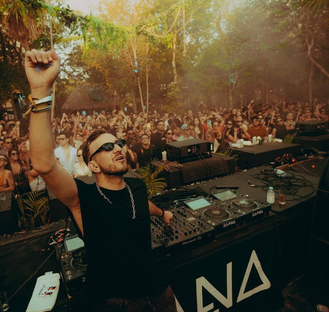 DJ performing at an outdoor stage surrounded by lush greenery and a crowd of dancing festivalgoers, embodying the immersive vibe of Masara Festival 2025 in Puglia.
