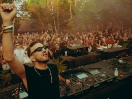 DJ performing at an outdoor stage surrounded by lush greenery and a crowd of dancing festivalgoers, embodying the immersive vibe of Masara Festival 2025 in Puglia.