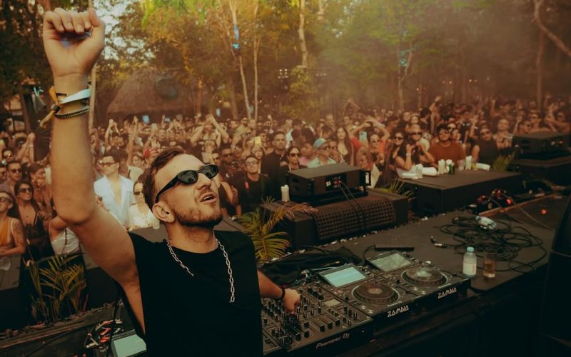DJ performing at an outdoor stage surrounded by lush greenery and a crowd of dancing festivalgoers, embodying the immersive vibe of Masara Festival 2025 in Puglia.