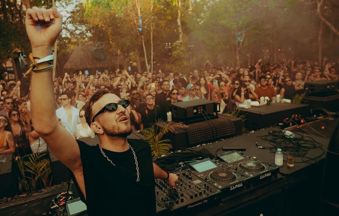 DJ performing at an outdoor stage surrounded by lush greenery and a crowd of dancing festivalgoers, embodying the immersive vibe of Masara Festival 2025 in Puglia.