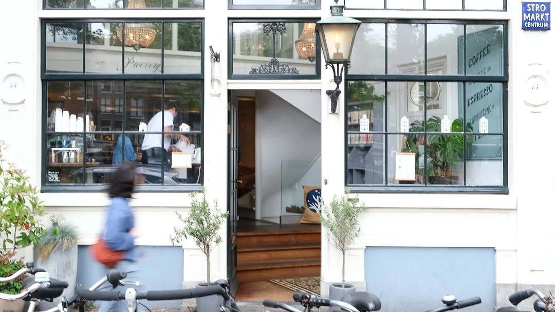 Exterior white facade of the Sango coffee shop with a woman walking in front of it and bikes parked.