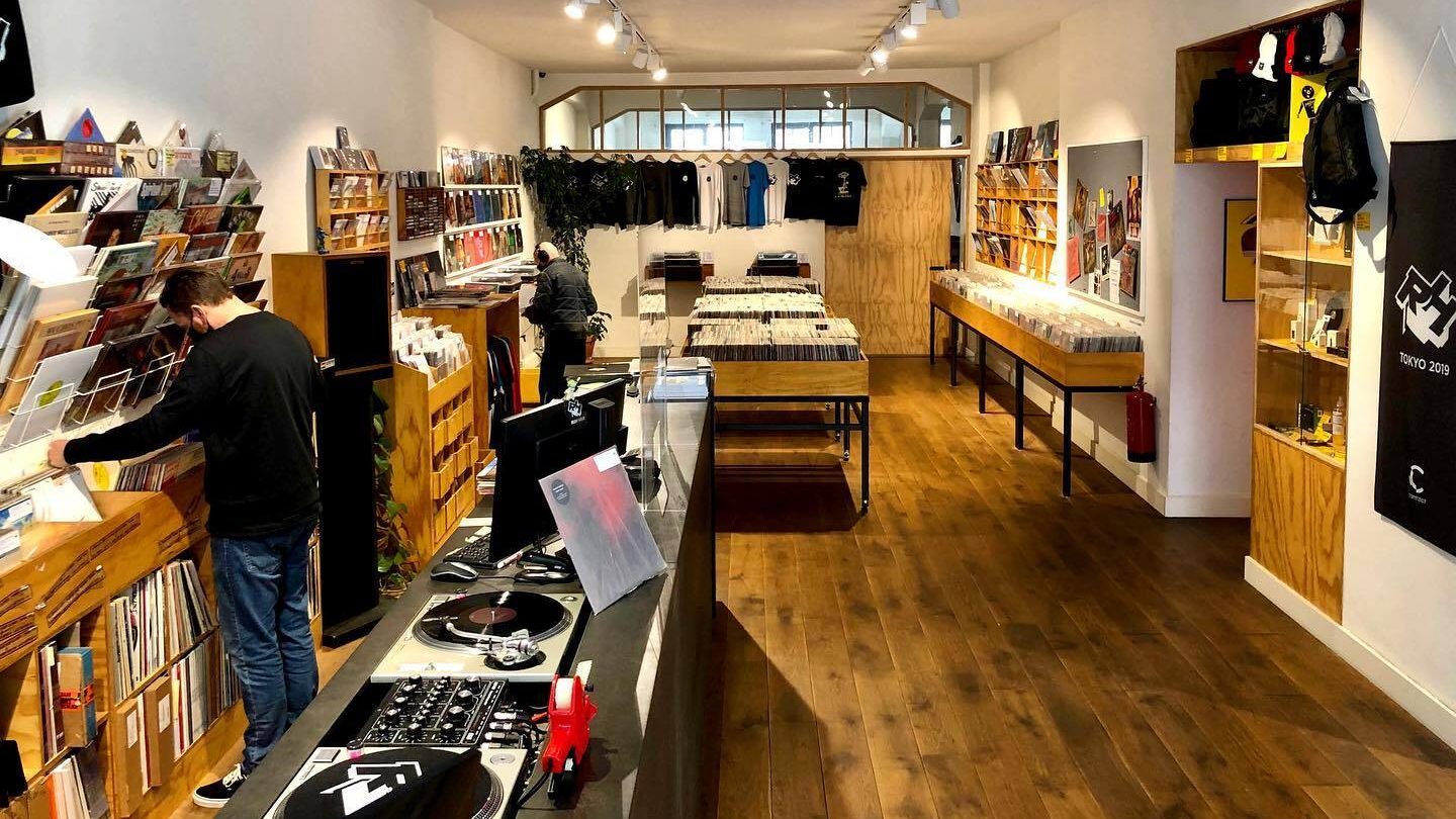 Brightly lit record store interior with rows of vinyl records and a DJ booth.