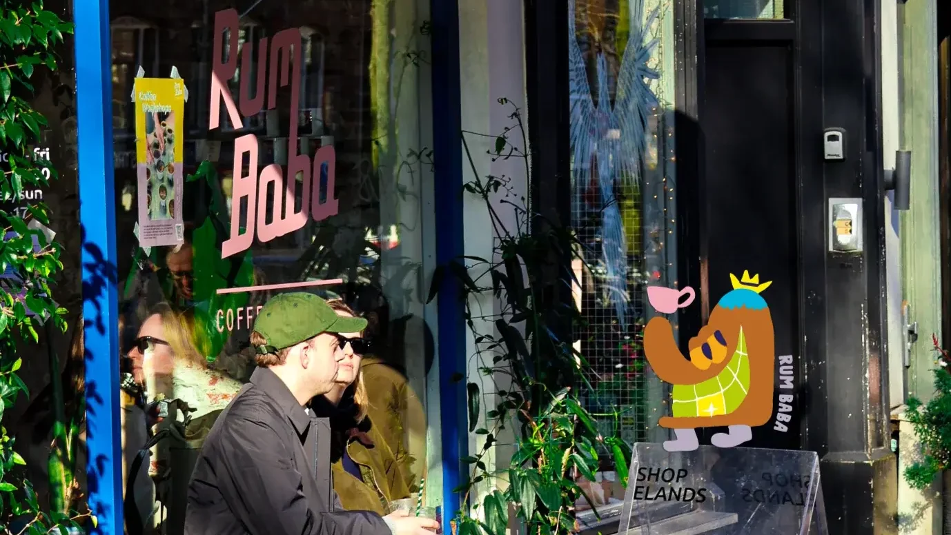 Two people sitting outside a coffee shop named Rum Baba on a sunny day.
