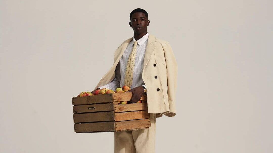 Man in a tailored suit holding wooden crates of fruit, inspired by fruit picking.