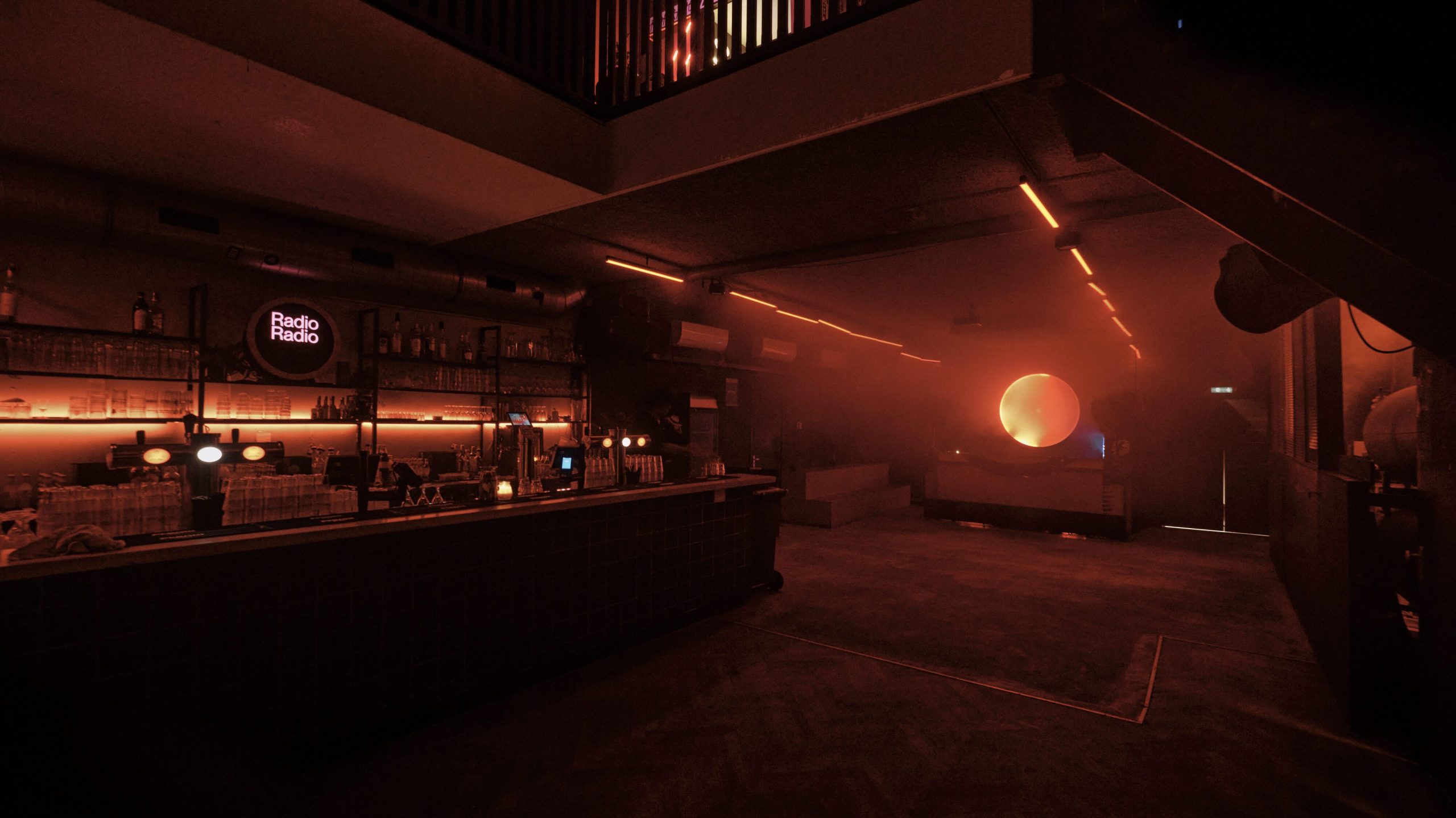 Bar and dimly lit red interior of Radio Radio club with circular neon light.