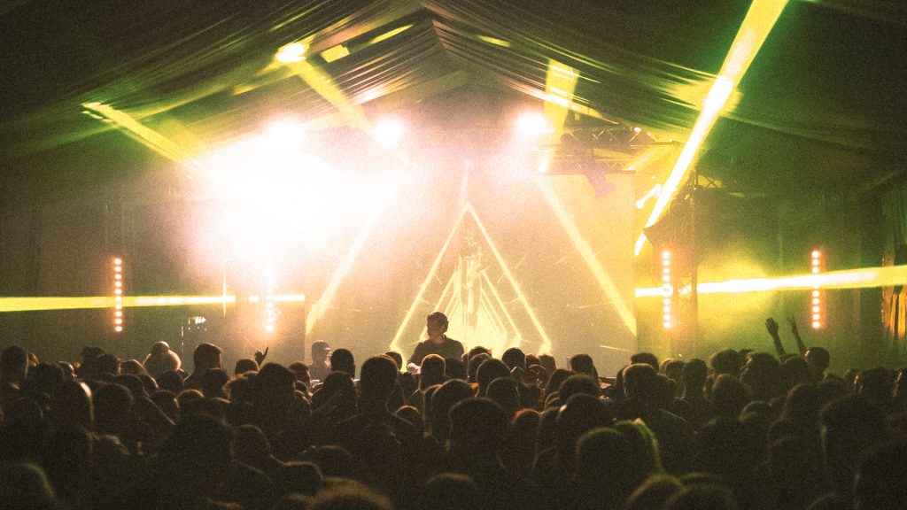 Foule compacte à Circolo Magnolia, scène avec visuels triangulaires et faisceaux vert-jaune sous un chapiteau.