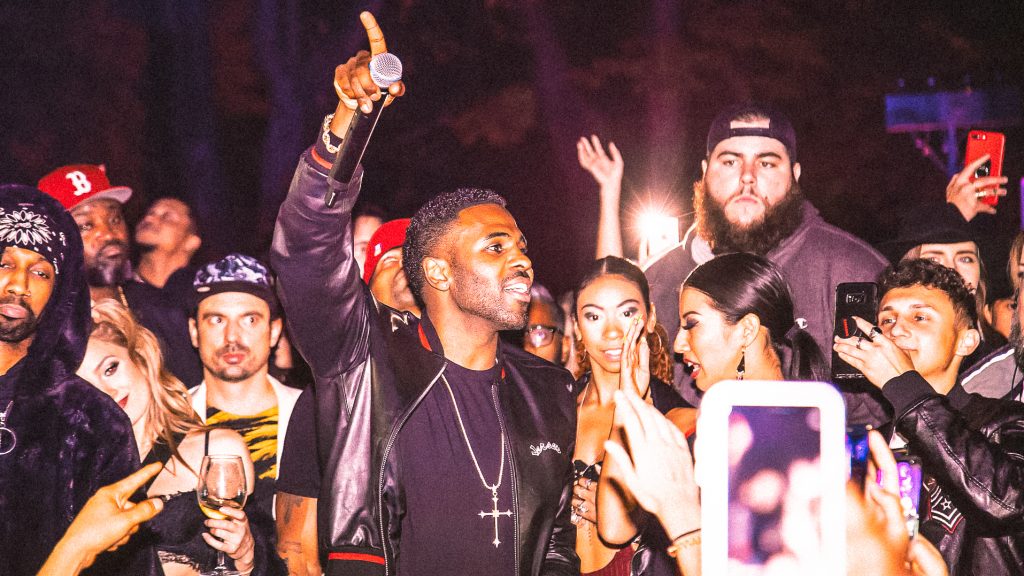 Performance au JUSTME Milano : chanteur micro levé au milieu de la foule, smartphones et flashes tout autour.