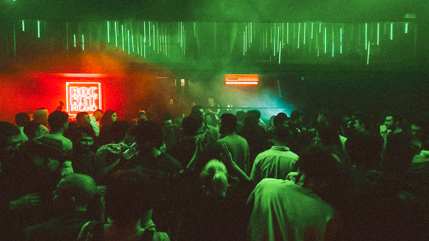 Foule compacte au ROCKET Milano, néon rouge « ROCKET » et plafond de LED vertes au-dessus du DJ booth enfumé.