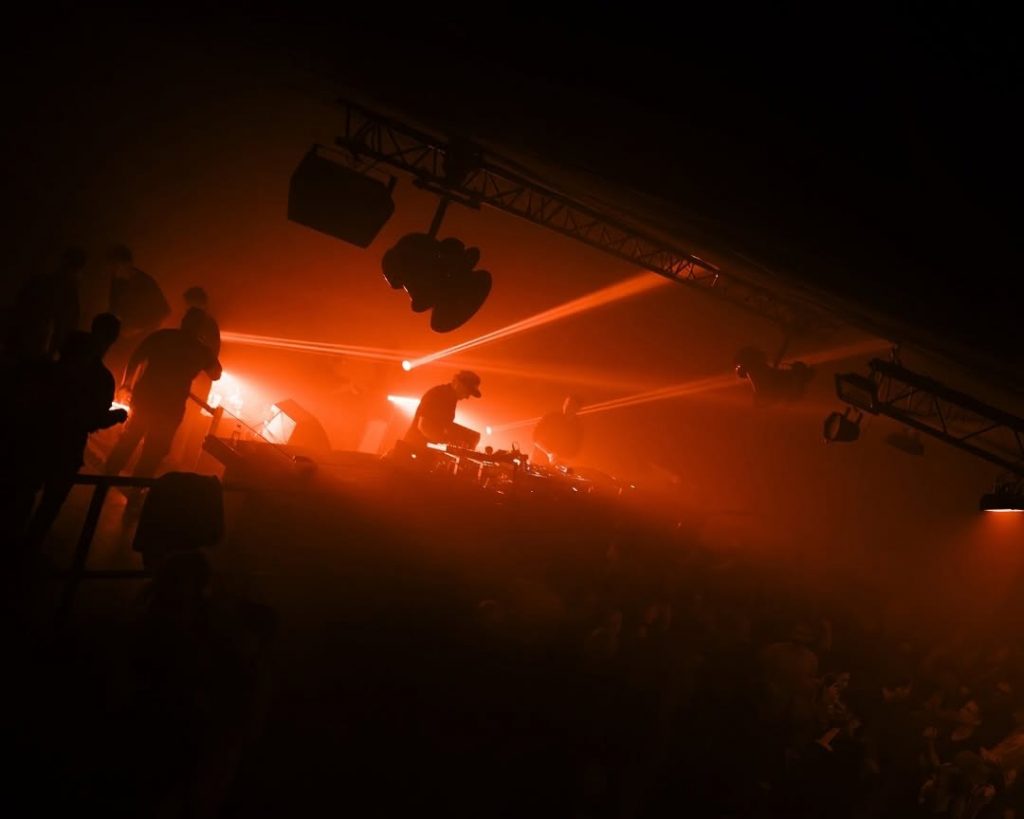Interior of La Rítmica Club in Valencia. A DJ mixes in front of crowd in a dark and foggy ambience