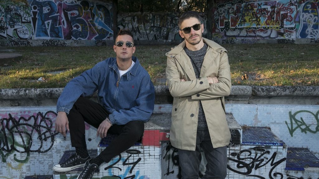 Dirty Channels posing in front of a park wall painted with graffiti.