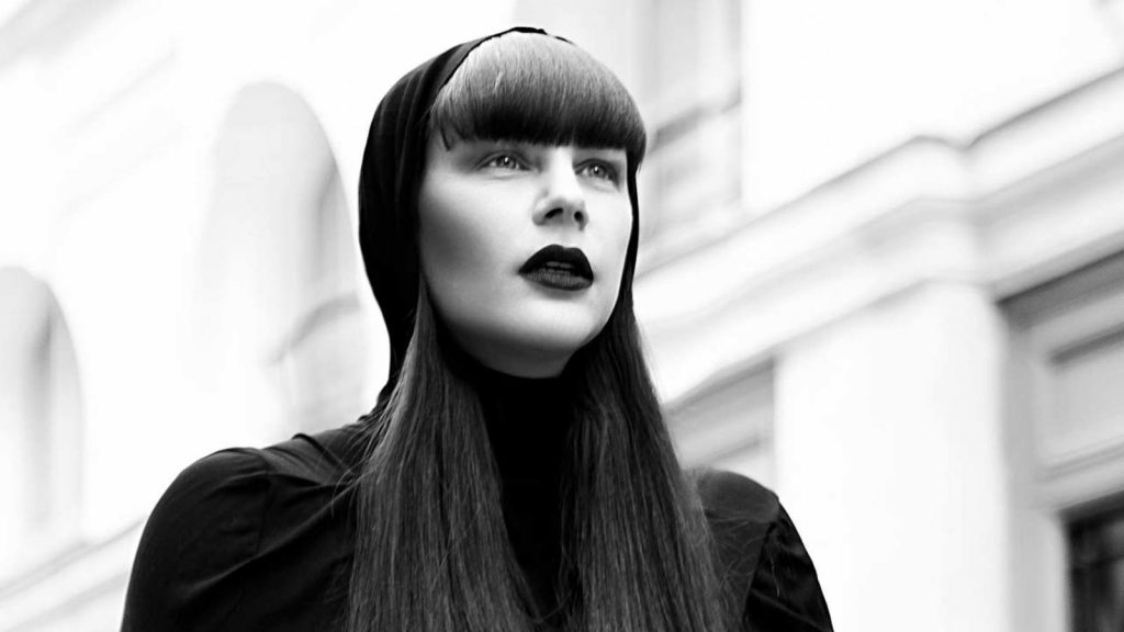 Image of DJ Miss Kittin wearing black lipstick and a black hood