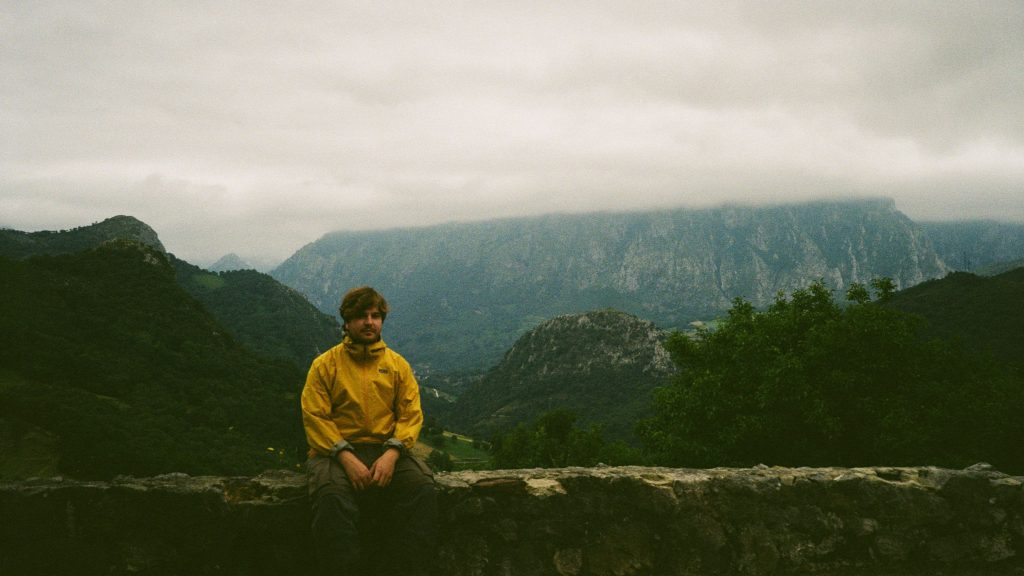 El DJ Pépe sentado en un muro bajito delante de paisaje montañoso