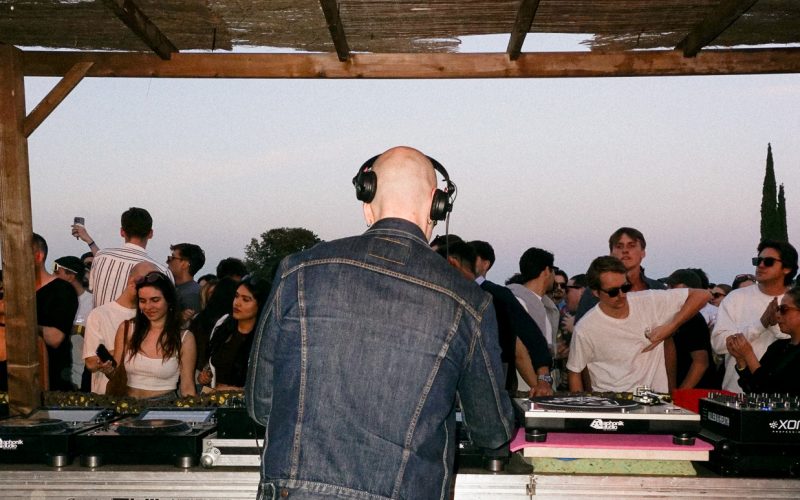 Photo from the back of a DJ booth while DJ is performing in a small open air festival