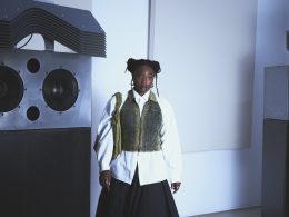 A woman named Kokoprisci posing in a white room in front of a hifi sound system