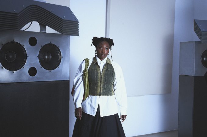 A woman named Kokoprisci posing in a white room in front of a hifi sound system